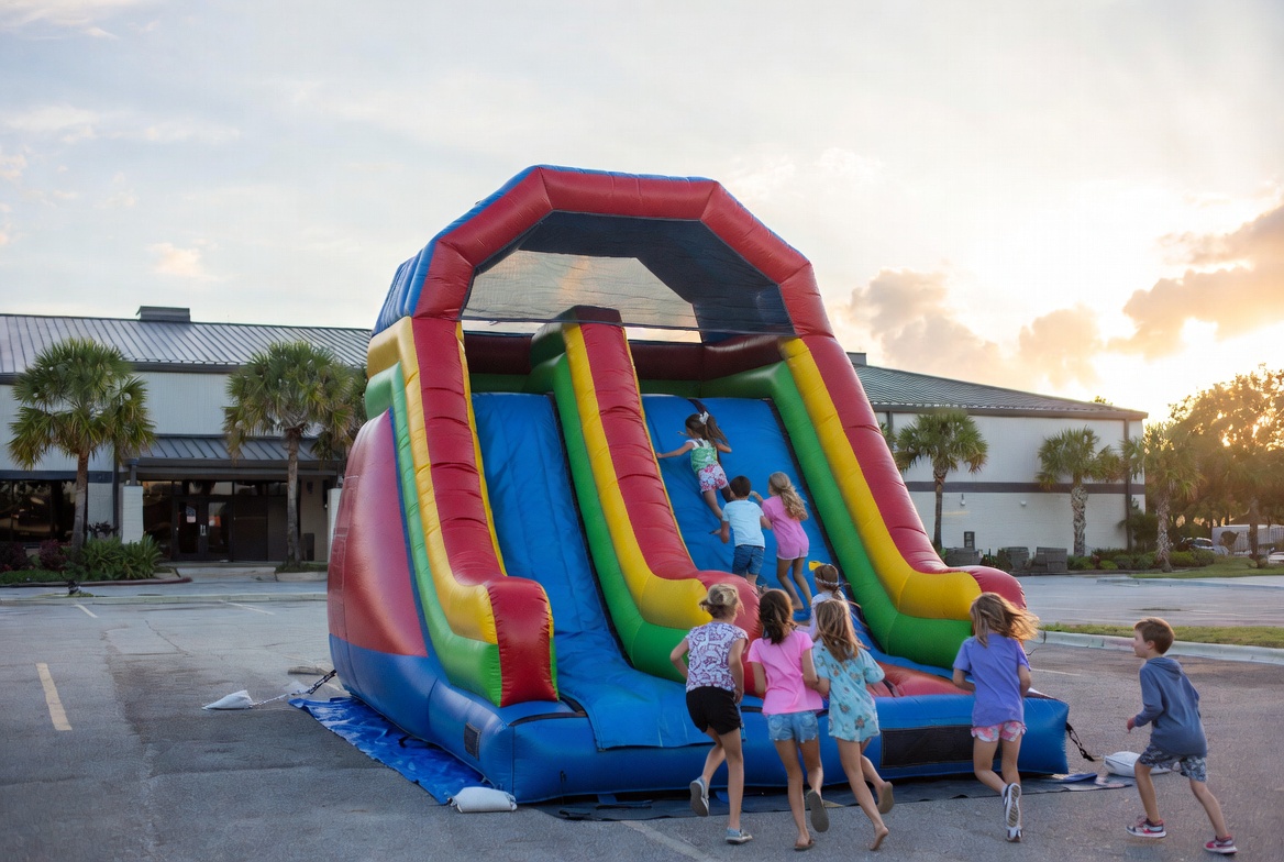 Children running toward a bounce house on a Cape Coral church parking lot during VBS week